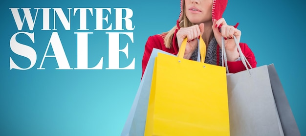 Composite image of blonde in winter clothes holding shopping bags