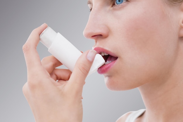 Composite image of blonde woman taking her inhaler