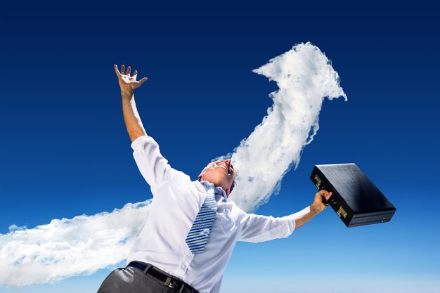 Composite image of businessman holding briefcase and cheering against cloud arrow