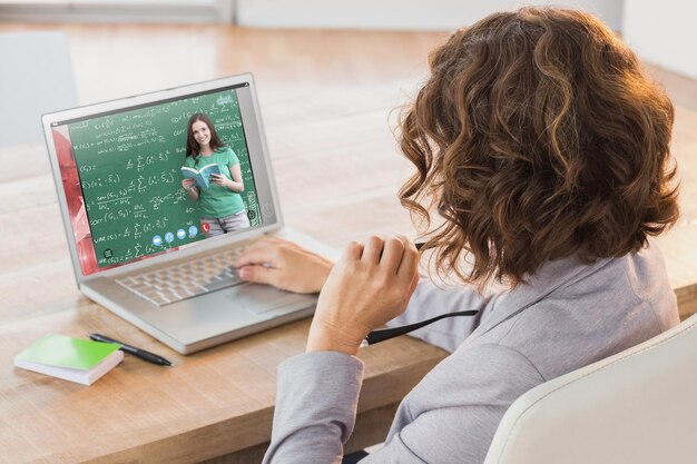 Composite image of businesswoman using laptop at desk in creative office