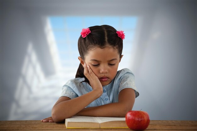 Composite image of concentrated girl reading book at desk