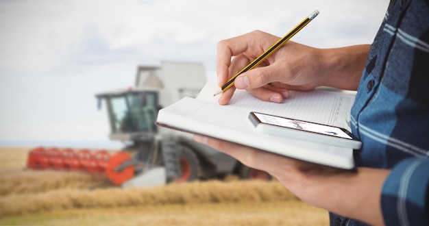 Composite image of cropped image of farmer writing with pencil on book