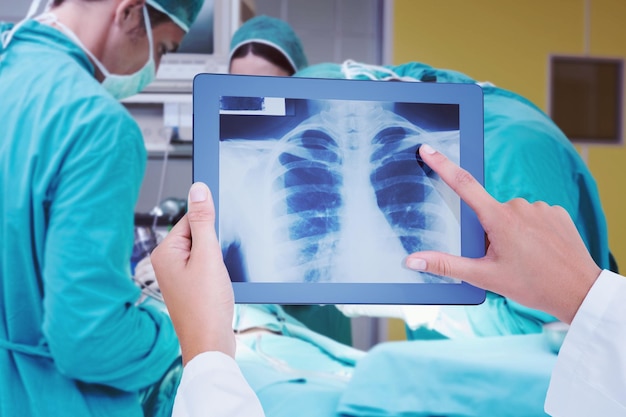 Composite image of doctor looking at xray on tablet