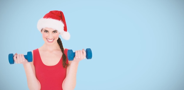 Composite image of festive fit brunette holding dumbbells