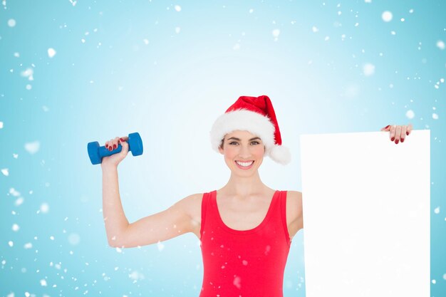 Composite image of festive fit brunette holding page and dumbbell