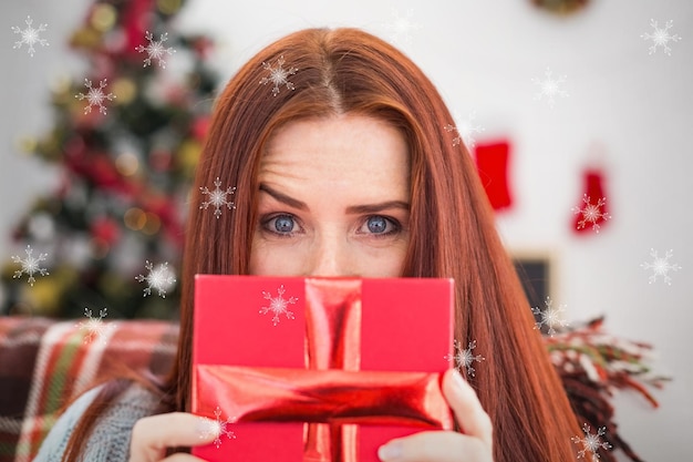 Composite image of festive redhead with gift on the couch