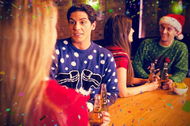 Composite image of friends having beers by table during christmas