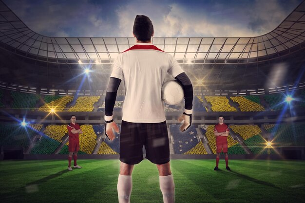 Composite image of goalie facing opposition against large football stadium with brasilian fans