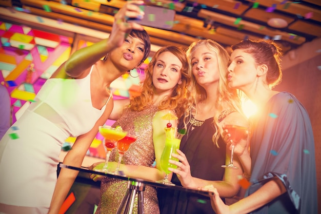 Composite image of group of friends taking selfie from mobile phone while having cocktail