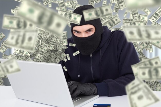 Composite image of hacker in balaclava hacking a laptop