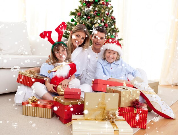 Composite image of happy family holding christmas gifts with snow falling