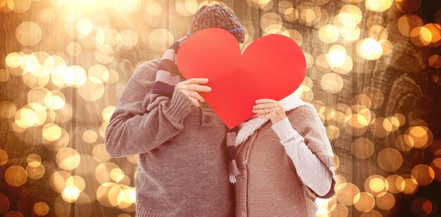 Composite image of happy mature couple in winter clothes holding red heart