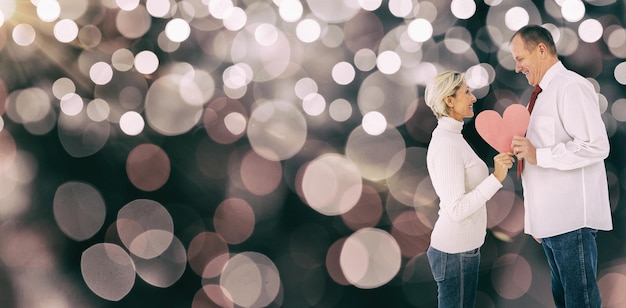 Composite image of older affectionate couple holding pink heart shape