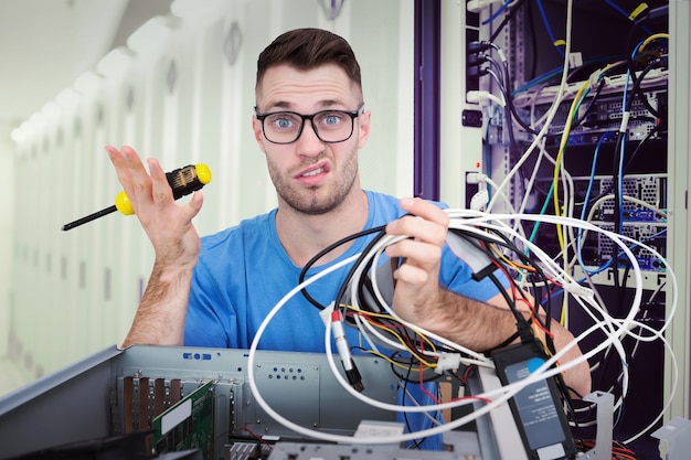 Composite image of portrait of confused it professional with screw driver and cables in front of ope