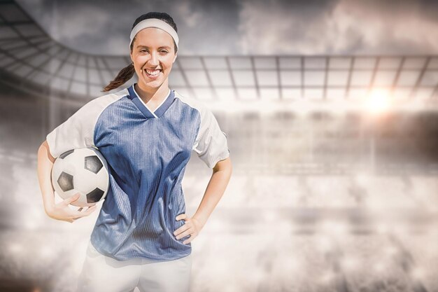 Composite image of portrait of happy woman football player holding a football