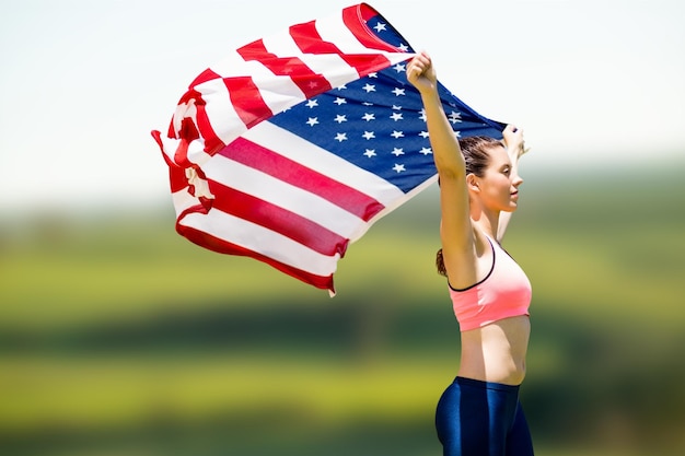 Composite image of profile view of sportswoman raising an american flag