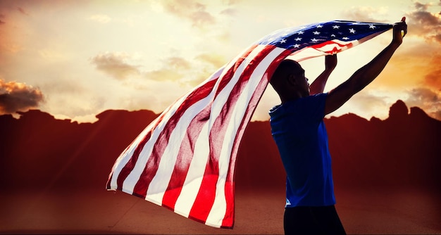 Composite image of rear view of sportsman raising an american flag