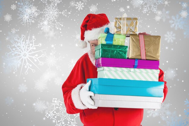 Composite image of santa claus hiding behind christmas presents