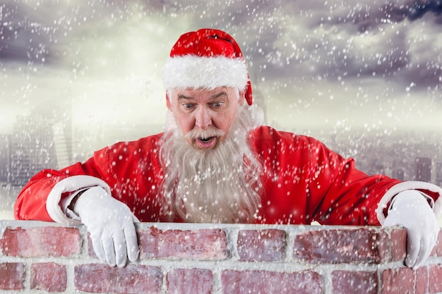 Composite image of santa claus peeking over wall