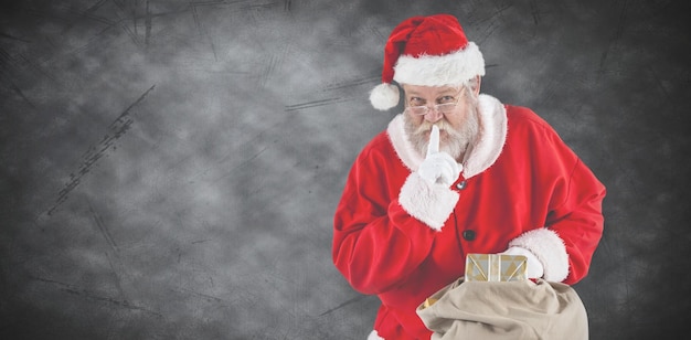 Composite image of santa claus with finger on lips and holding a gifts