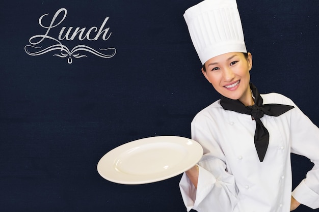 Composite image of smiling female cook holding empty plate in kitchen