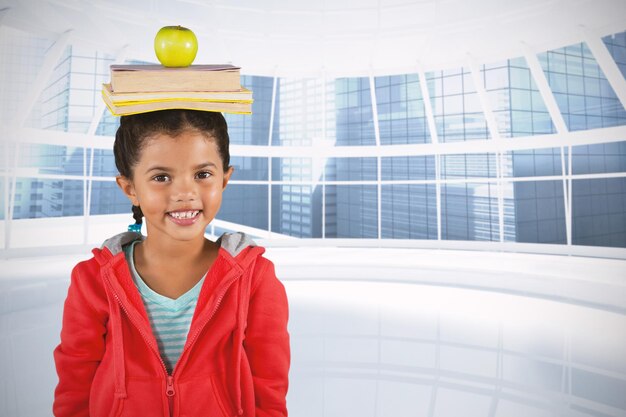 Composite image of smiling girl balancing books and apple on head