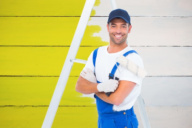 Composite image of smiling handyman with paint roller standing by ladder