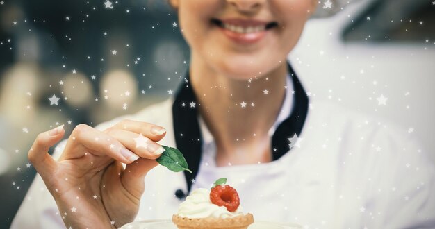 Composite image of smiling head chef putting mint leaf on little cake on plate