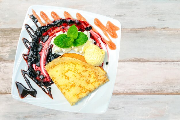 Composite image of a sweet dessert pancakes with ice cream whipped cream and mint on a bright wooden table top view