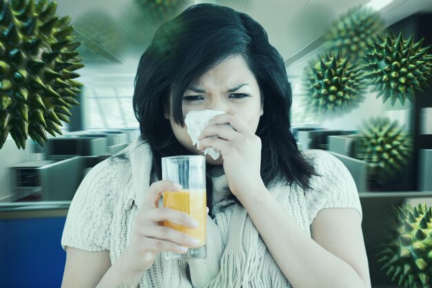 Composite image of woman holding a glass of orange juice while sneezing