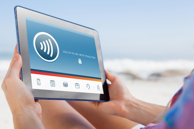 Composite image of woman sitting on beach in deck chair using tablet pc