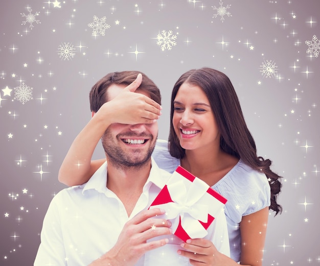 Composite image of woman surprising boyfriend with gift against grey vignette