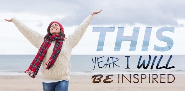 Composite image of woman in warm clothing stretching arms on beach