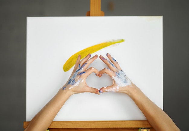 Composition of artist hands making heart shape sign over picture canvas