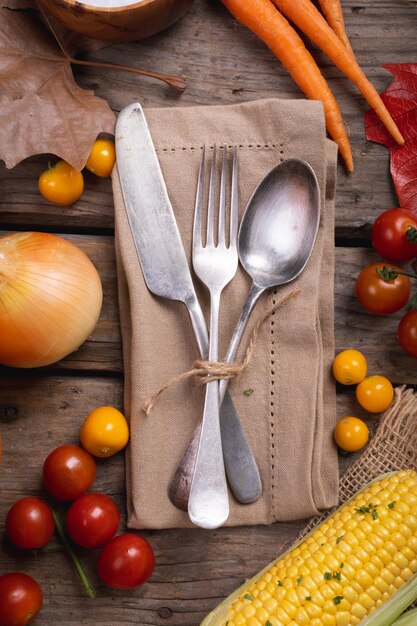 Composition of autumn halloween carrots, corn, tomatoes and cutlery on wood. autumn, halloween tradition, food, cooking and celebration concept.