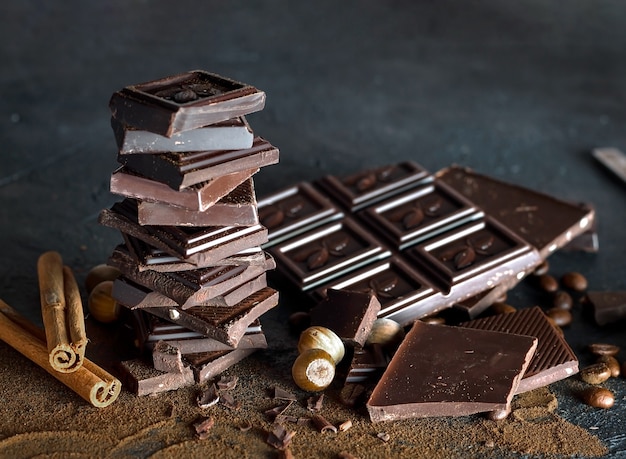 Composizione di barrette e pezzi di diverso latte e cioccolato fondente, cacao grattugiato su fondo marrone.