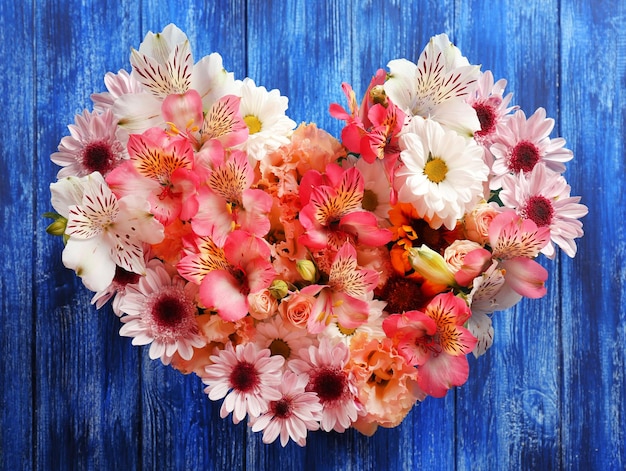 Photo composition of beautiful flowers in a heart shape on blue wooden background