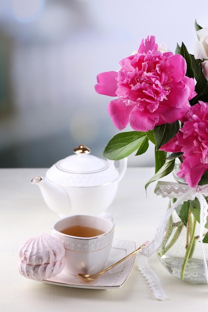 Composition of beautiful peonies in vase, tea in cup and marshmallow, on table, on light background