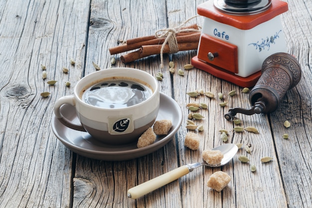 Composition of black hot coffee in a cup, brown sugar, coffee beans and cardamon seeds on a wooden table. Special light.