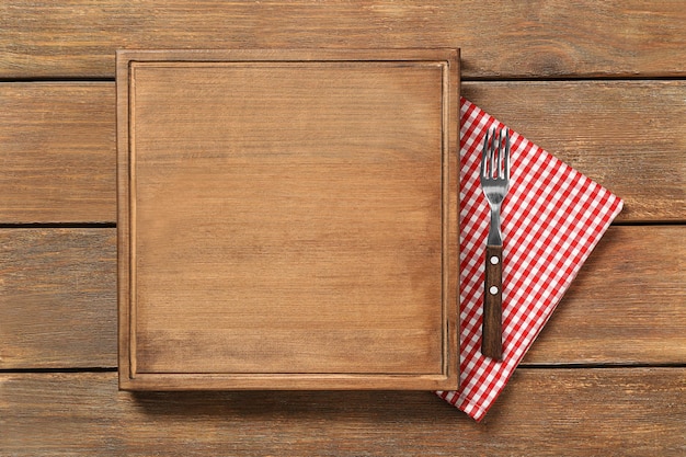 Composition of board fork and napkin on wooden background