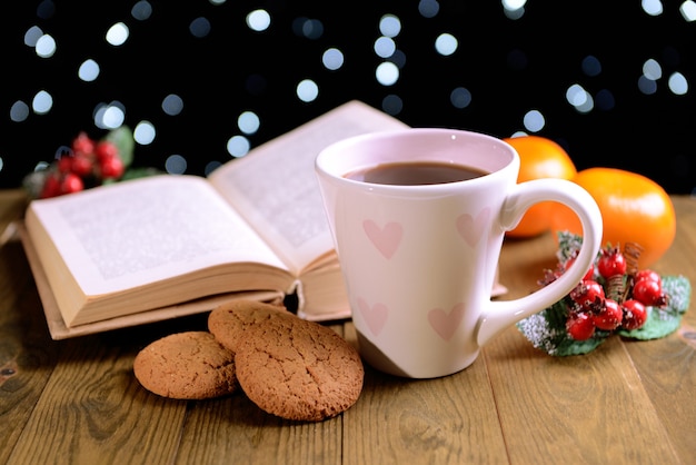 Composition of book with cup of coffee and Christmas decorations on table on dark background