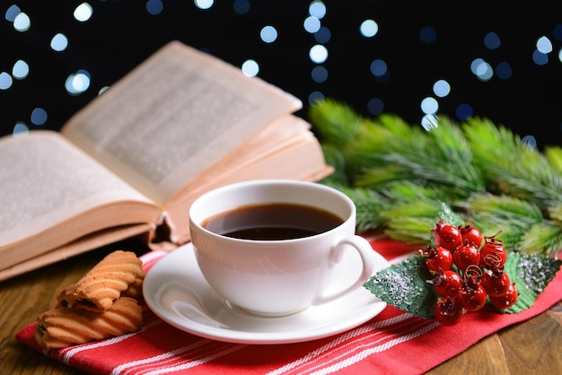 Composition of book with cup of coffee and Christmas decorations on table on dark background