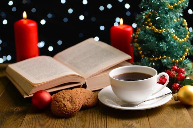 Composition of book with cup of coffee and Christmas decorations on table on dark background