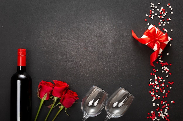 Composizione di una bottiglia di vino, due bicchieri e una confezione regalo con un fiocco rosso su uno sfondo scuro. san valentino, appuntamento, amore.