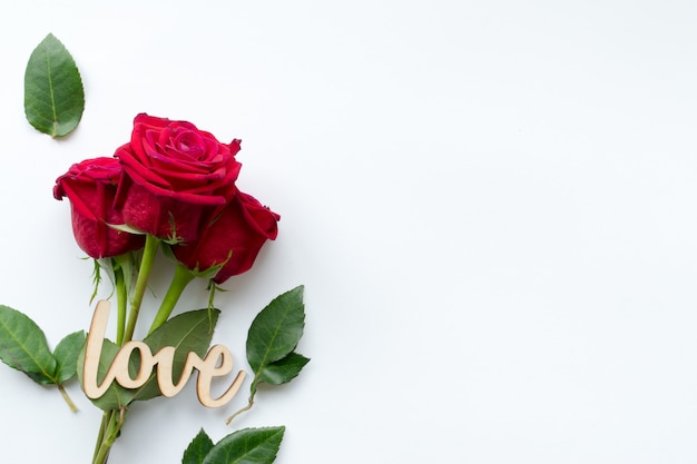 Composition of bouquet of red roses and decorative wooden word love on white background