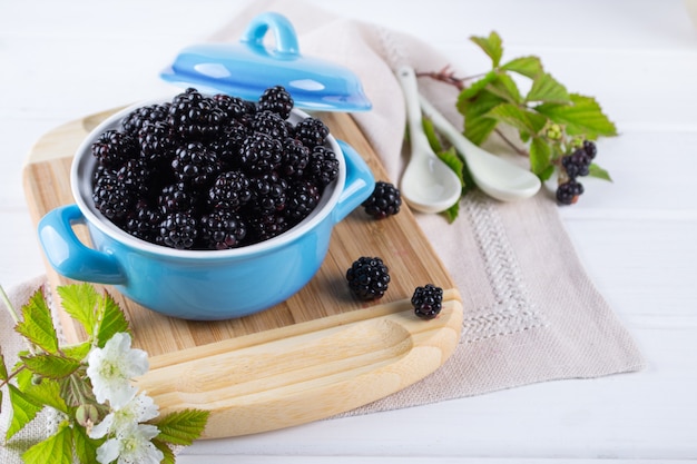 Composition of branch of Blackberry with leaf and  blackberries in a blue ceramic bowl on white table.