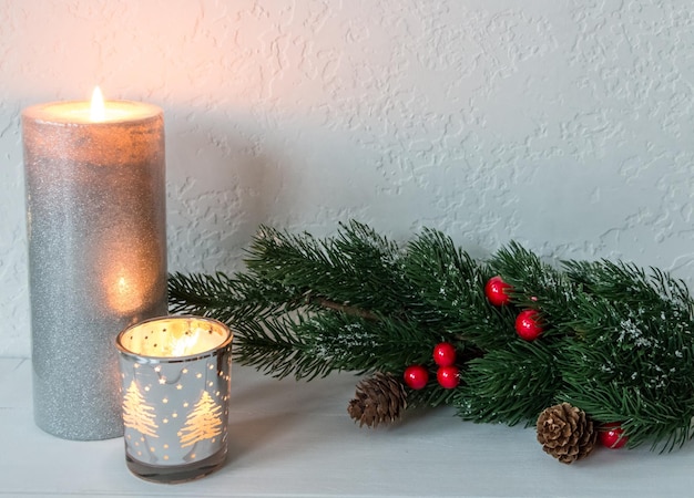 Photo composition of candles and tree branches decorated with snow cones and red berries on a white background