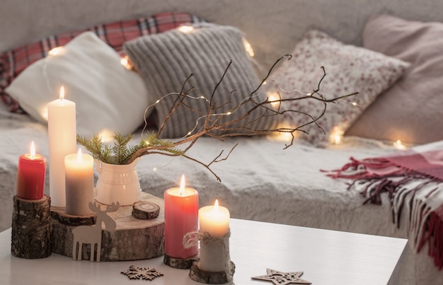 Composition of candles on white table near sofa with pillows