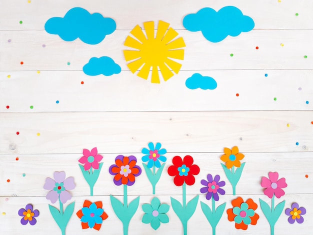 Composition of colorful summer flowers, sun, clouds from multi-colored paper, step by step. Child make crafts his own hands. Cute DIY handmade art creativity on a wooden table. Top view, copy space