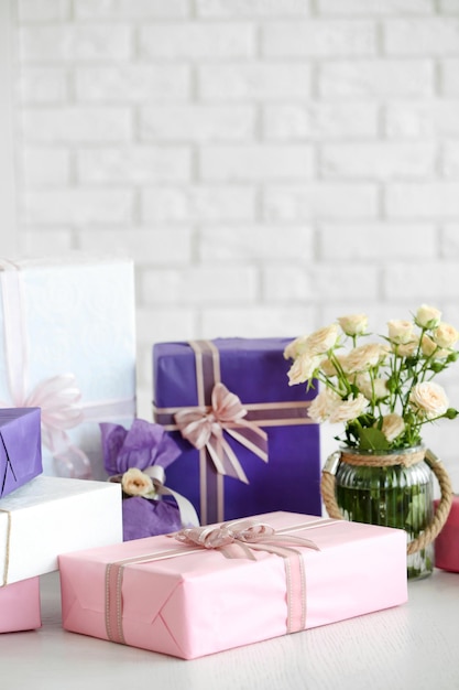 Композиция из красочных подарочных коробок и цветов в стекле на белом столе на фоне кирпичной стены